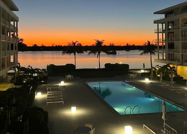 pool at dusk with a water view and a patio area