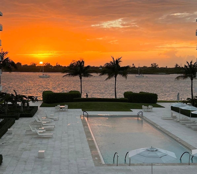 pool at dusk featuring a patio area and a water view