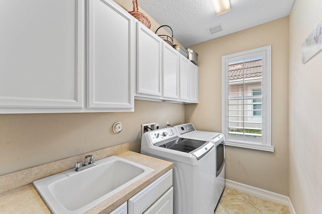 clothes washing area with cabinets, a textured ceiling, sink, light tile patterned floors, and washing machine and dryer