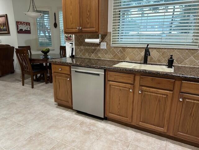 kitchen featuring hanging light fixtures, light tile patterned flooring, dark stone counters, stainless steel dishwasher, and sink