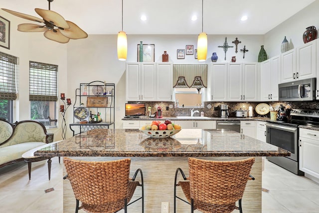 kitchen with a kitchen island, dark stone countertops, appliances with stainless steel finishes, a healthy amount of sunlight, and ceiling fan