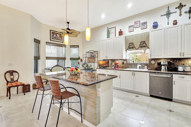 kitchen featuring dark stone counters, backsplash, a center island, ceiling fan, and stainless steel dishwasher