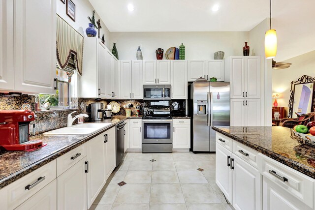 kitchen featuring white cabinets, backsplash, dark stone countertops, stainless steel appliances, and sink