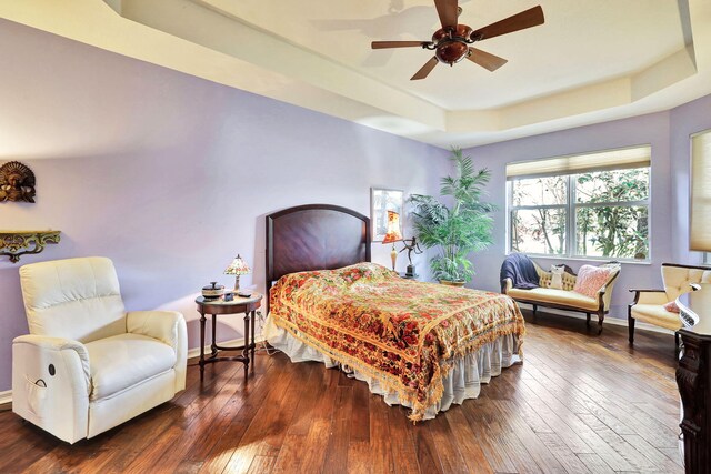 bedroom with a raised ceiling, ceiling fan, and dark hardwood / wood-style floors