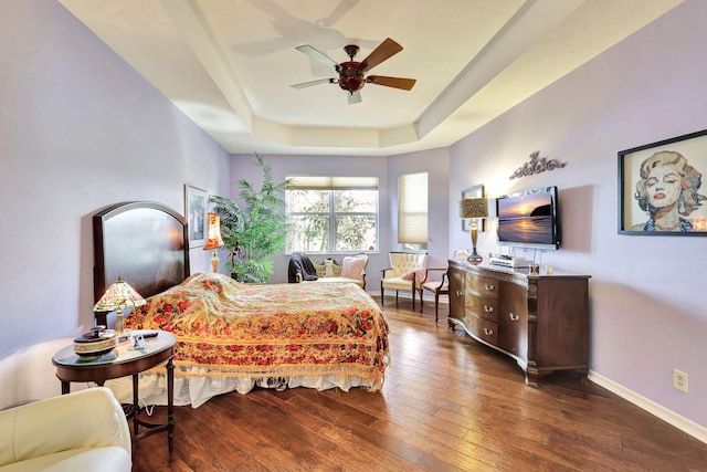 bedroom with dark wood-type flooring, ceiling fan, and a tray ceiling