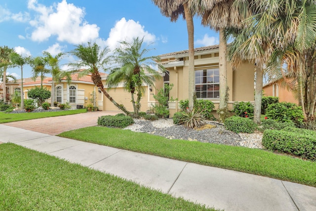 mediterranean / spanish-style home featuring an attached garage, a tile roof, decorative driveway, and stucco siding