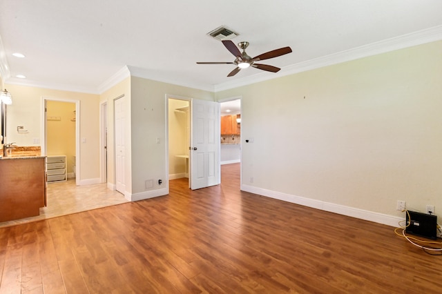 unfurnished bedroom featuring a spacious closet, hardwood / wood-style floors, crown molding, ensuite bathroom, and ceiling fan