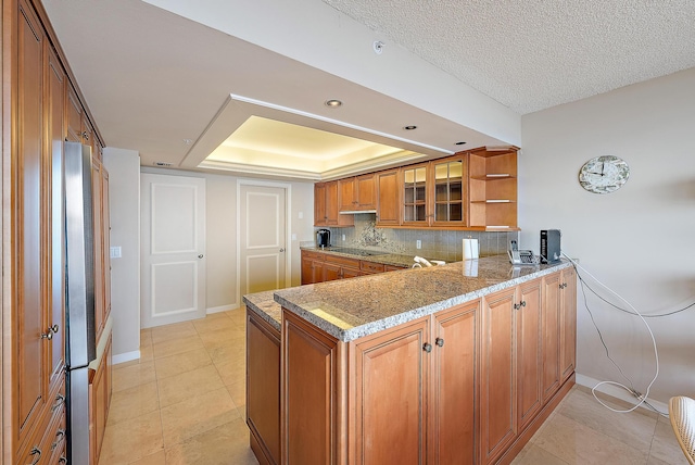 kitchen featuring black electric cooktop, light stone countertops, tasteful backsplash, a raised ceiling, and kitchen peninsula