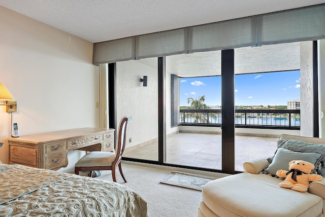 bedroom with a textured ceiling, a water view, and light carpet