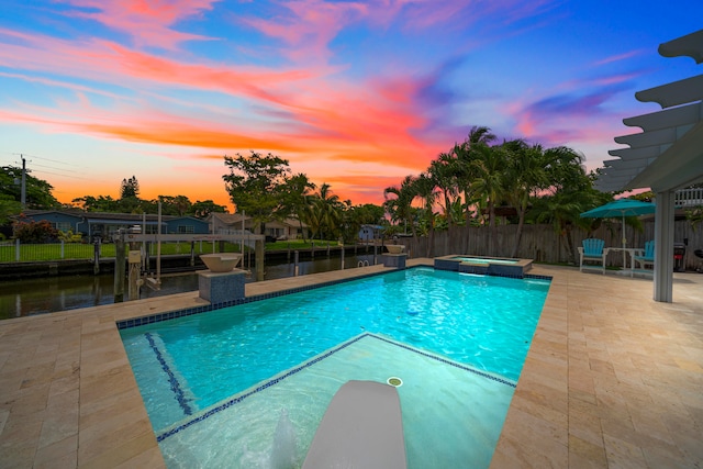 pool at dusk featuring a patio area, an in ground hot tub, and a water view