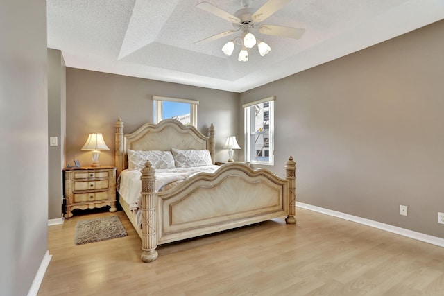 bedroom with ceiling fan, a raised ceiling, a textured ceiling, and light hardwood / wood-style flooring