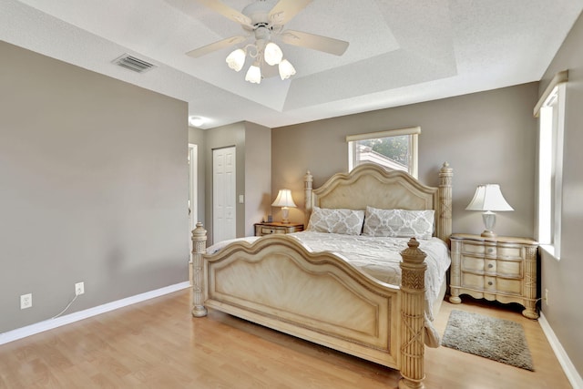 bedroom with a textured ceiling, a raised ceiling, ceiling fan, light hardwood / wood-style floors, and a closet