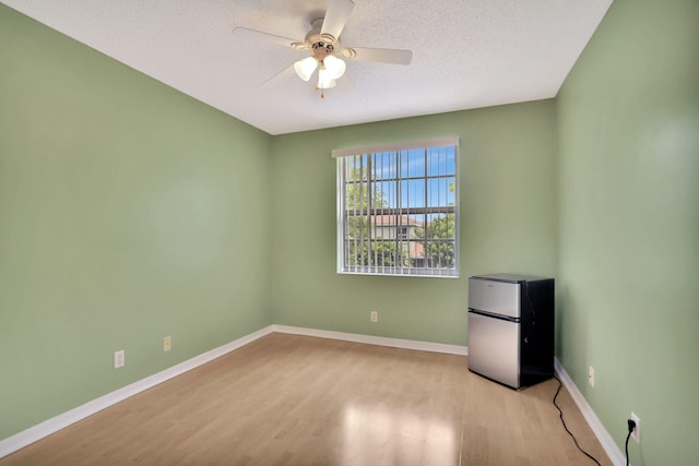 empty room with ceiling fan, light hardwood / wood-style flooring, and a textured ceiling