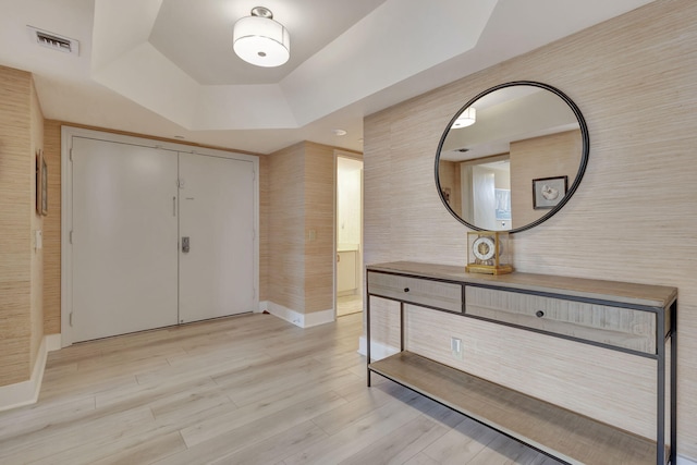 foyer entrance with a tray ceiling and light hardwood / wood-style floors