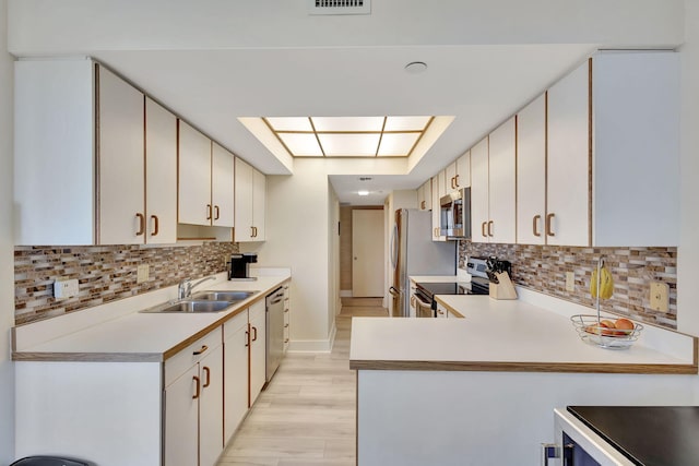 kitchen with a skylight, sink, white cabinets, backsplash, and stainless steel appliances