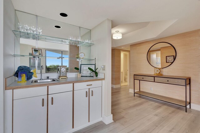 bar with light wood-type flooring, sink, and white cabinets