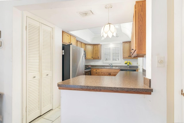 kitchen with kitchen peninsula, stainless steel refrigerator, light tile patterned flooring, sink, and decorative light fixtures