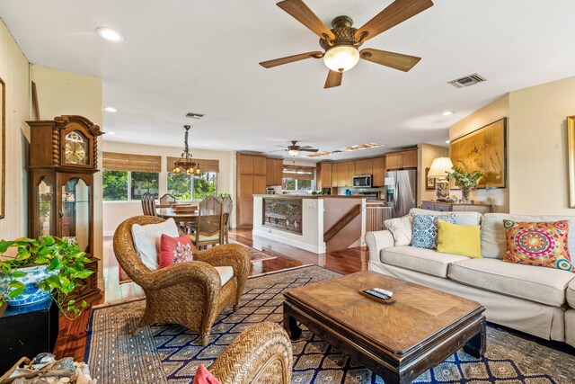 living room with ceiling fan with notable chandelier and hardwood / wood-style floors