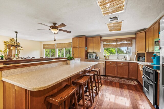 kitchen with decorative light fixtures, dark wood-type flooring, ceiling fan, a breakfast bar area, and stainless steel appliances