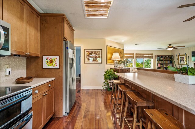 kitchen featuring appliances with stainless steel finishes, backsplash, dark hardwood / wood-style floors, a breakfast bar area, and ceiling fan