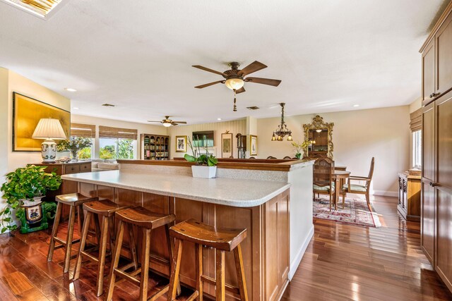 kitchen featuring decorative light fixtures, dark hardwood / wood-style floors, a kitchen island, ceiling fan, and a breakfast bar