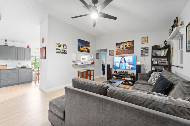 living room with ceiling fan, a textured ceiling, lofted ceiling, and light hardwood / wood-style flooring