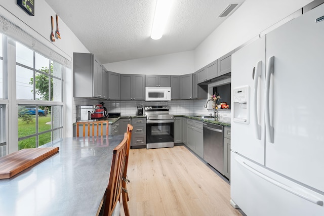 kitchen with decorative backsplash, gray cabinetry, stainless steel appliances, a textured ceiling, and lofted ceiling