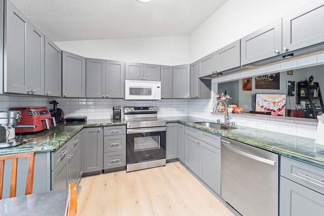 kitchen with light hardwood / wood-style floors, tasteful backsplash, gray cabinets, stainless steel appliances, and sink