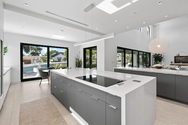 kitchen featuring gray cabinets, a spacious island, decorative light fixtures, light tile patterned floors, and black electric stovetop