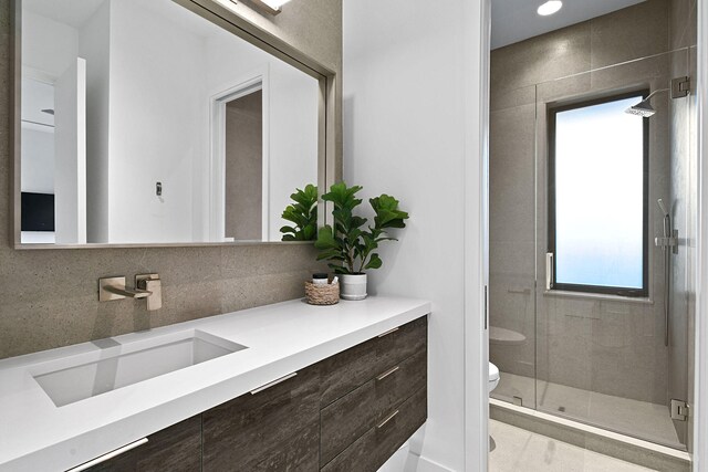 bathroom with toilet, decorative backsplash, vanity, and a shower with shower door