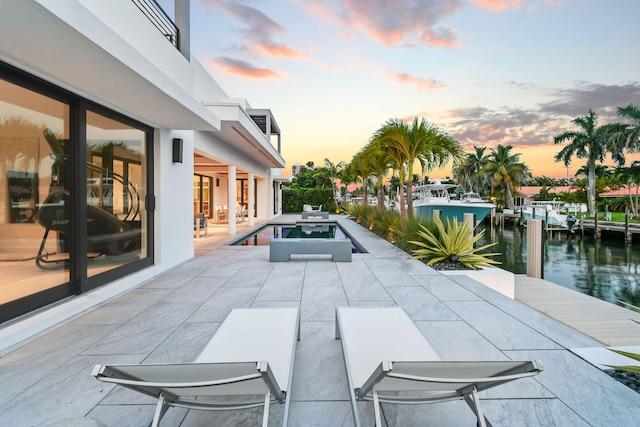 pool at dusk with a water view, an in ground hot tub, a patio, and a dock