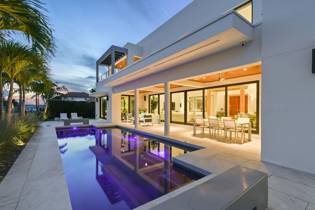 pool at dusk with outdoor lounge area, a patio, and ceiling fan