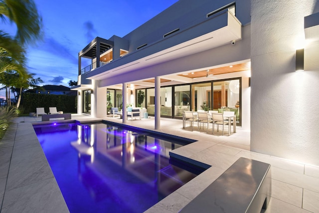 pool at dusk featuring ceiling fan, an outdoor hangout area, and a patio