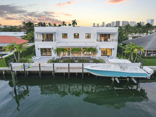 back house at dusk featuring a water view, a patio, a balcony, and a swimming pool