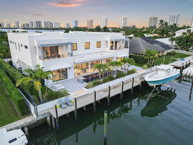 back house at dusk featuring an outdoor bar, a water view, and a patio