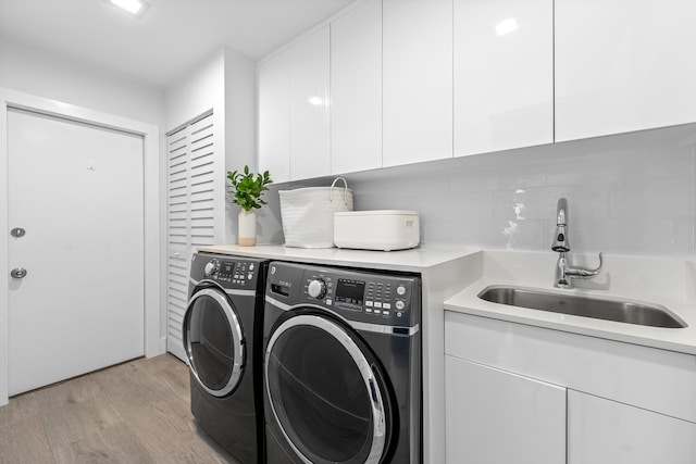 clothes washing area with sink, washer and dryer, light hardwood / wood-style flooring, and cabinets