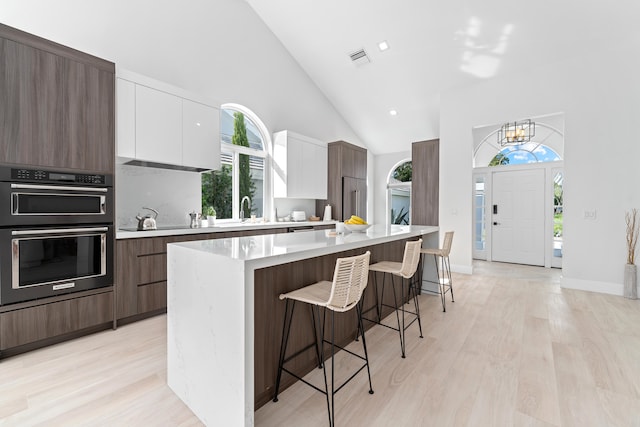 kitchen featuring a kitchen breakfast bar, light hardwood / wood-style flooring, stainless steel double oven, white cabinetry, and sink