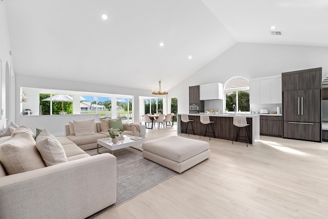 living room featuring a wealth of natural light, high vaulted ceiling, light hardwood / wood-style floors, and a notable chandelier