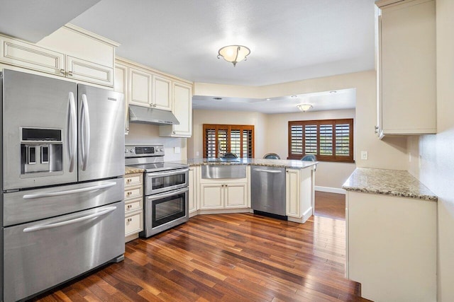 kitchen featuring appliances with stainless steel finishes, a peninsula, cream cabinetry, under cabinet range hood, and a sink