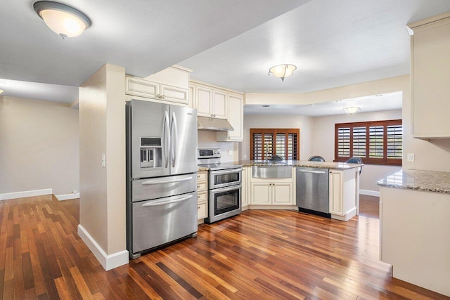 kitchen with stainless steel appliances, cream cabinetry, under cabinet range hood, and a peninsula