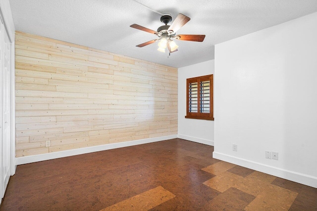 empty room featuring a ceiling fan, wood walls, a textured ceiling, and baseboards