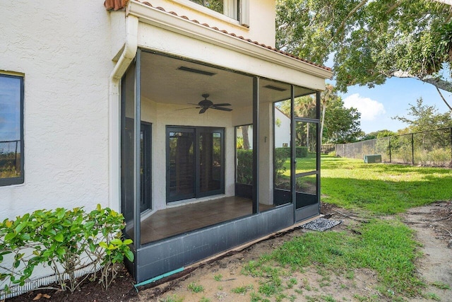 entrance to property with ceiling fan, fence, a tiled roof, a lawn, and stucco siding