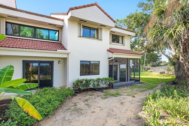 back of house featuring a sunroom, a tiled roof, and stucco siding