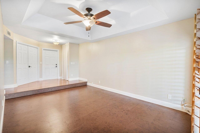 unfurnished room featuring a ceiling fan, a raised ceiling, visible vents, and baseboards