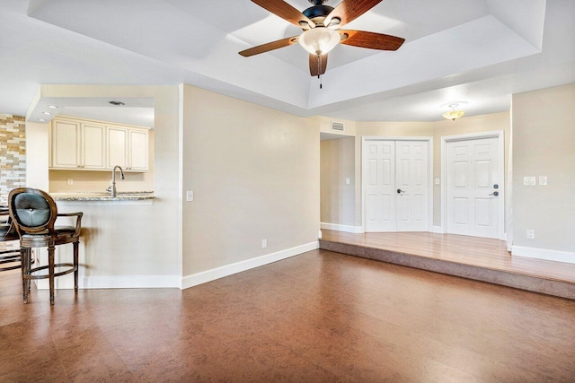 interior space with ceiling fan, a tray ceiling, visible vents, and baseboards