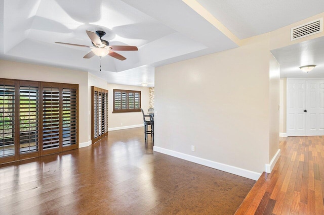 unfurnished room with baseboards, visible vents, a tray ceiling, and wood finished floors