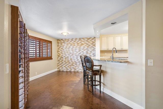 kitchen featuring baseboards, light stone counters, a breakfast bar, cream cabinetry, and a sink