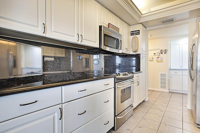 kitchen with tasteful backsplash, dark stone counters, ornamental molding, stainless steel appliances, and white cabinetry