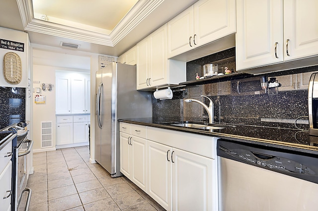 kitchen featuring dark countertops, a raised ceiling, appliances with stainless steel finishes, white cabinets, and a sink