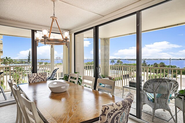 dining space with expansive windows, a water view, an inviting chandelier, and a healthy amount of sunlight